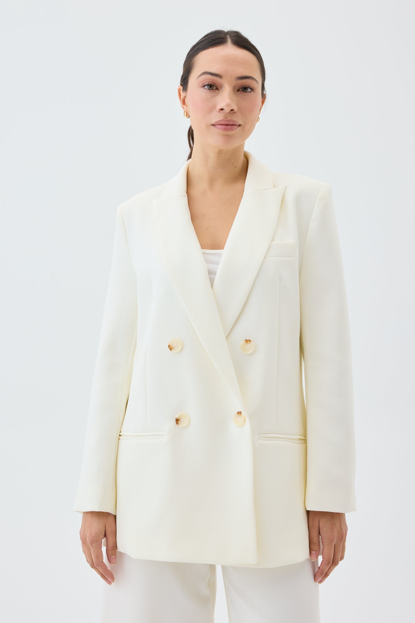 Woman wearing a white blazer with shell buttons on a plain background