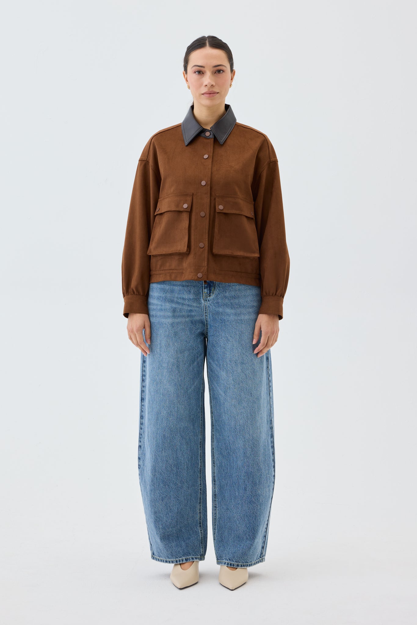 Person wearing a brown jacket with a collar and blue jeans on a white background