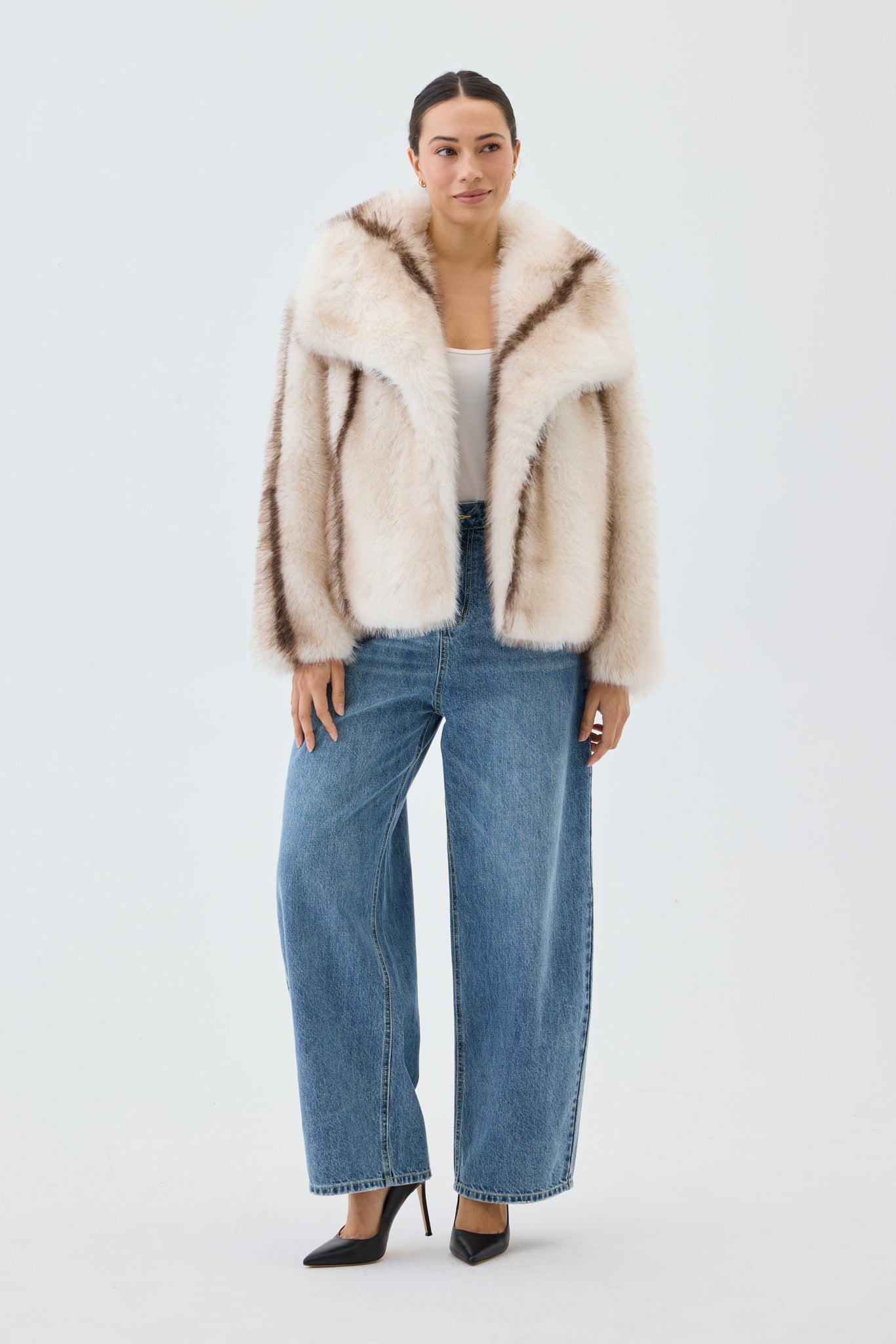 Woman wearing a fur coat, white top, and blue jeans on a white background