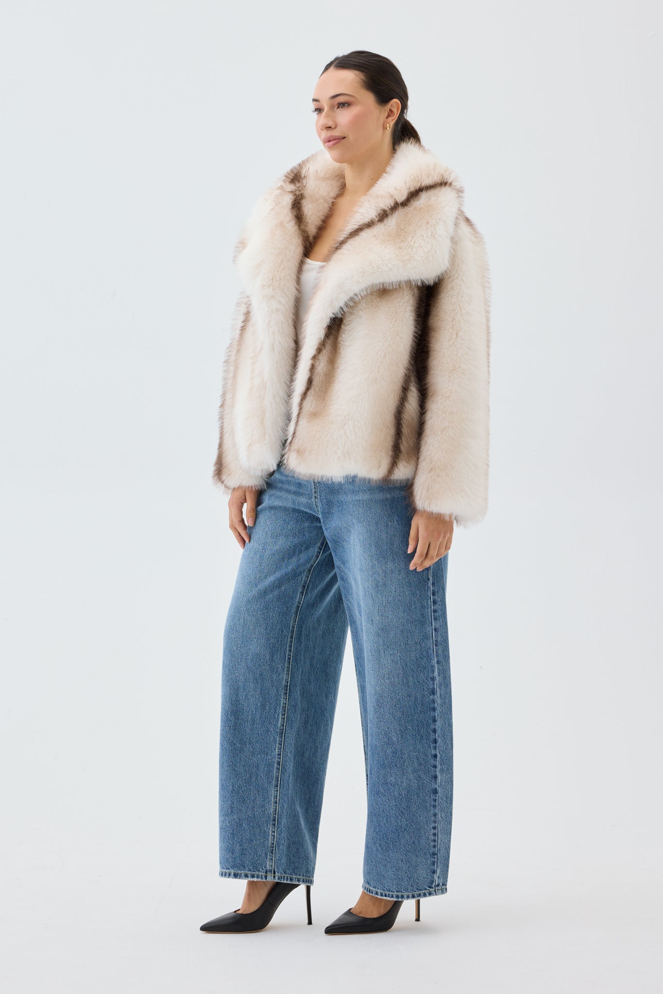 Woman wearing a cream fur coat and blue jeans on a white background