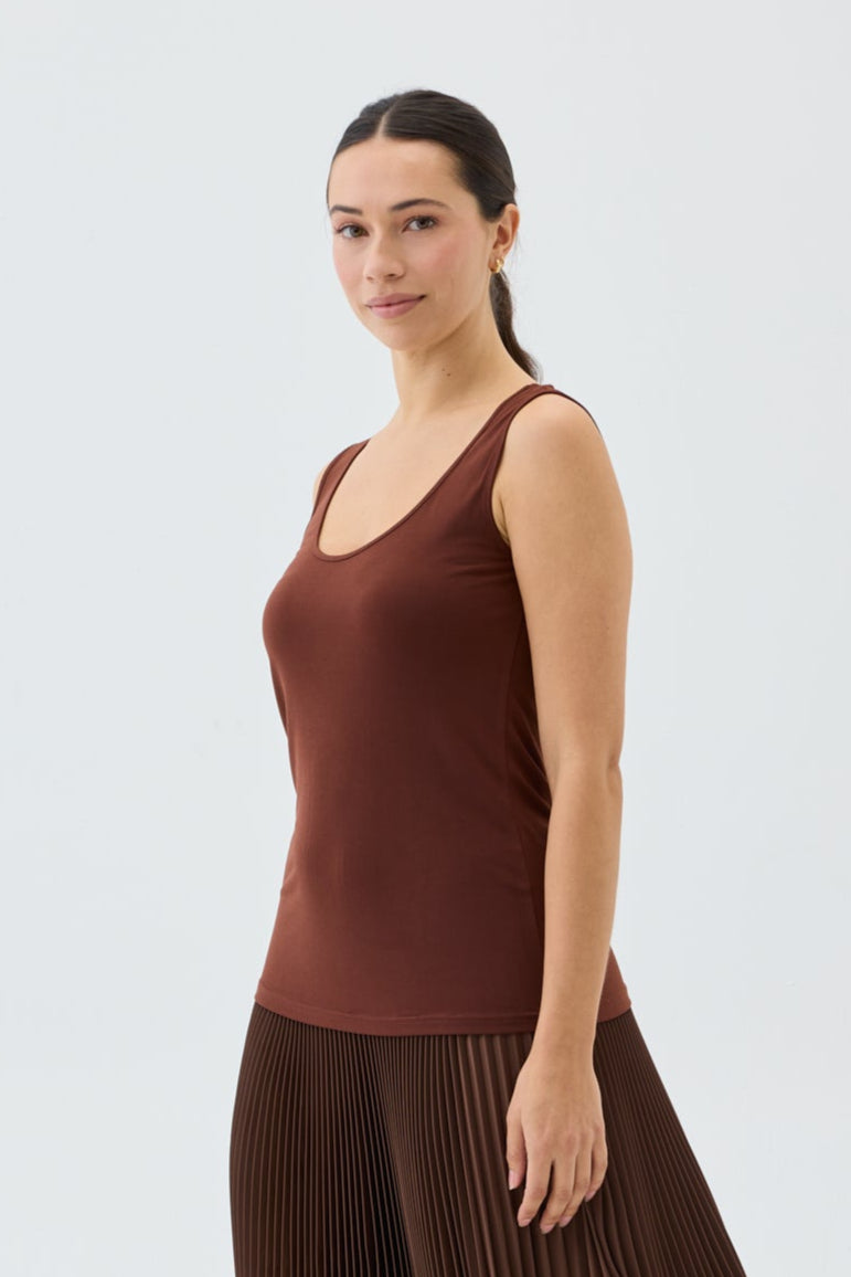 Woman wearing a brown sleeveless top and pleated skirt on a white background