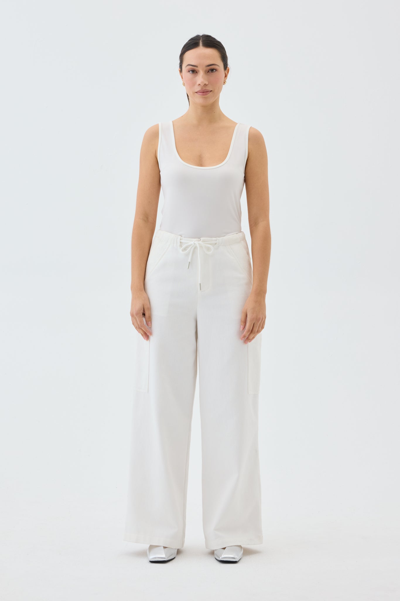Woman wearing a white tank top and wide leg cargo pants on a light gray background
