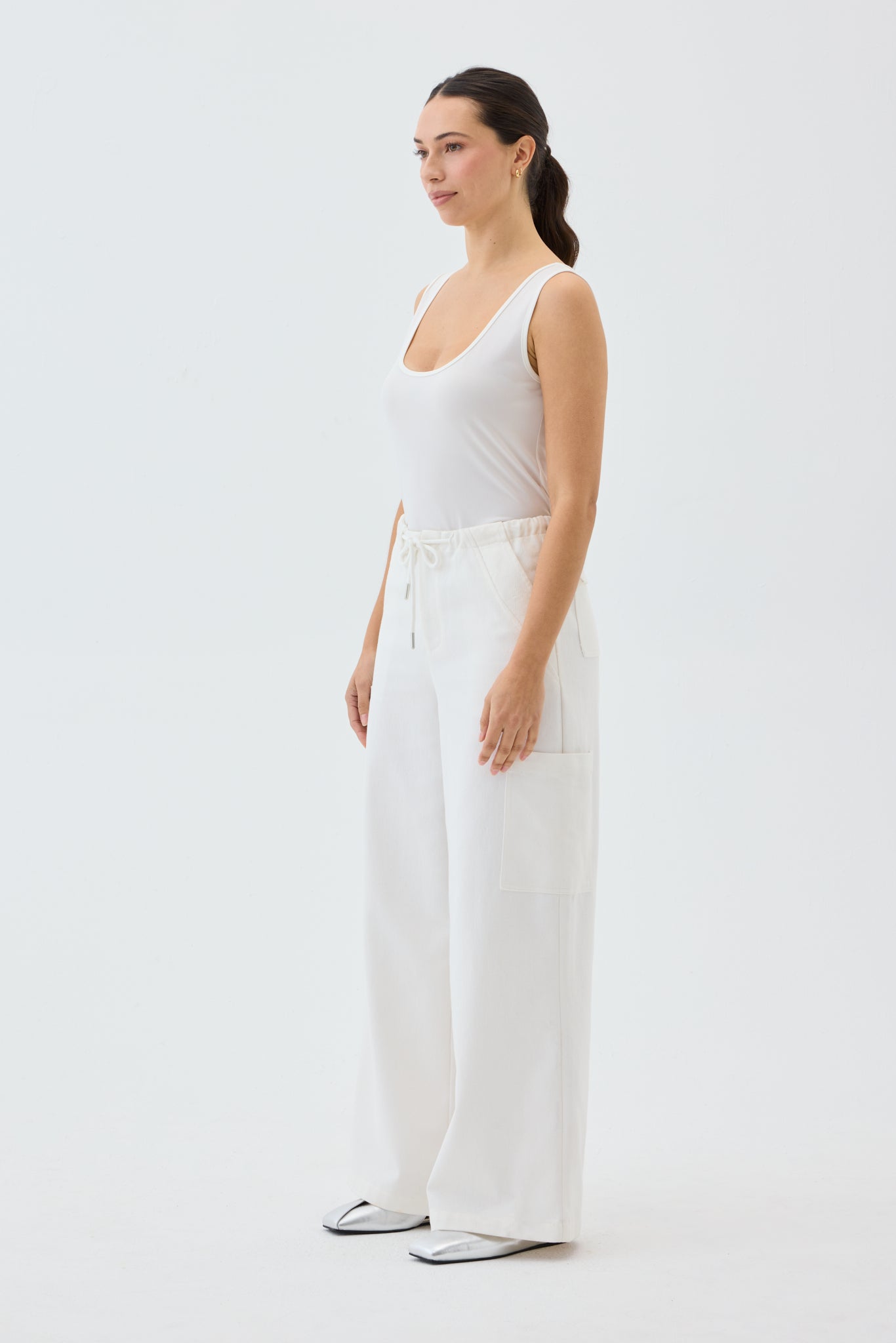 Woman wearing a white tank top and wide leg cargo pants on a light gray background