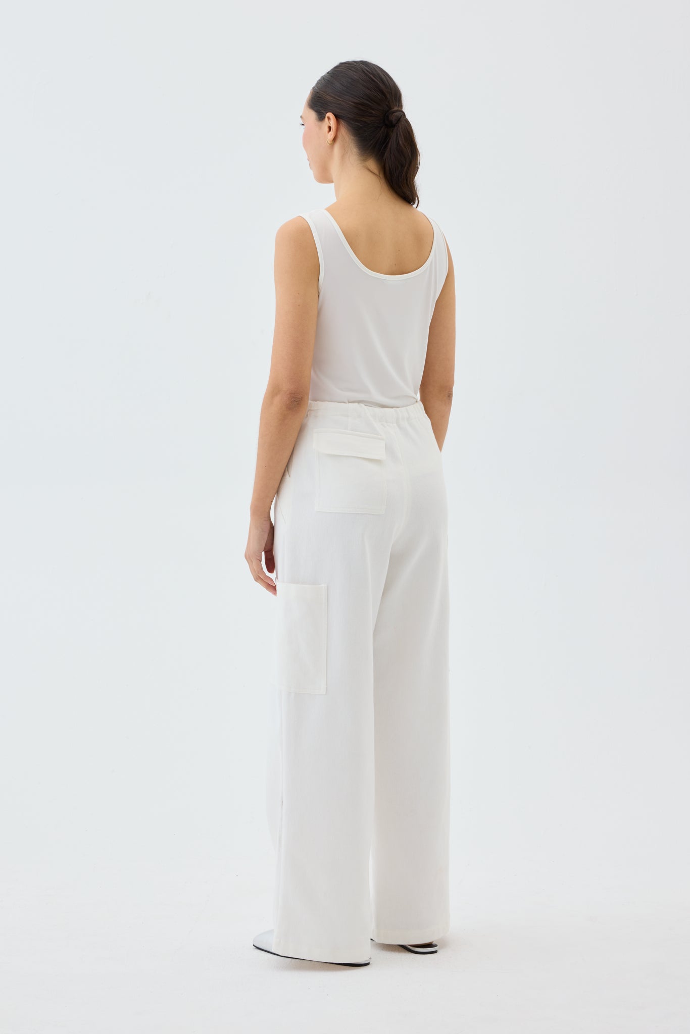 Woman wearing a white tank top and wide leg cargo pants on a light gray background