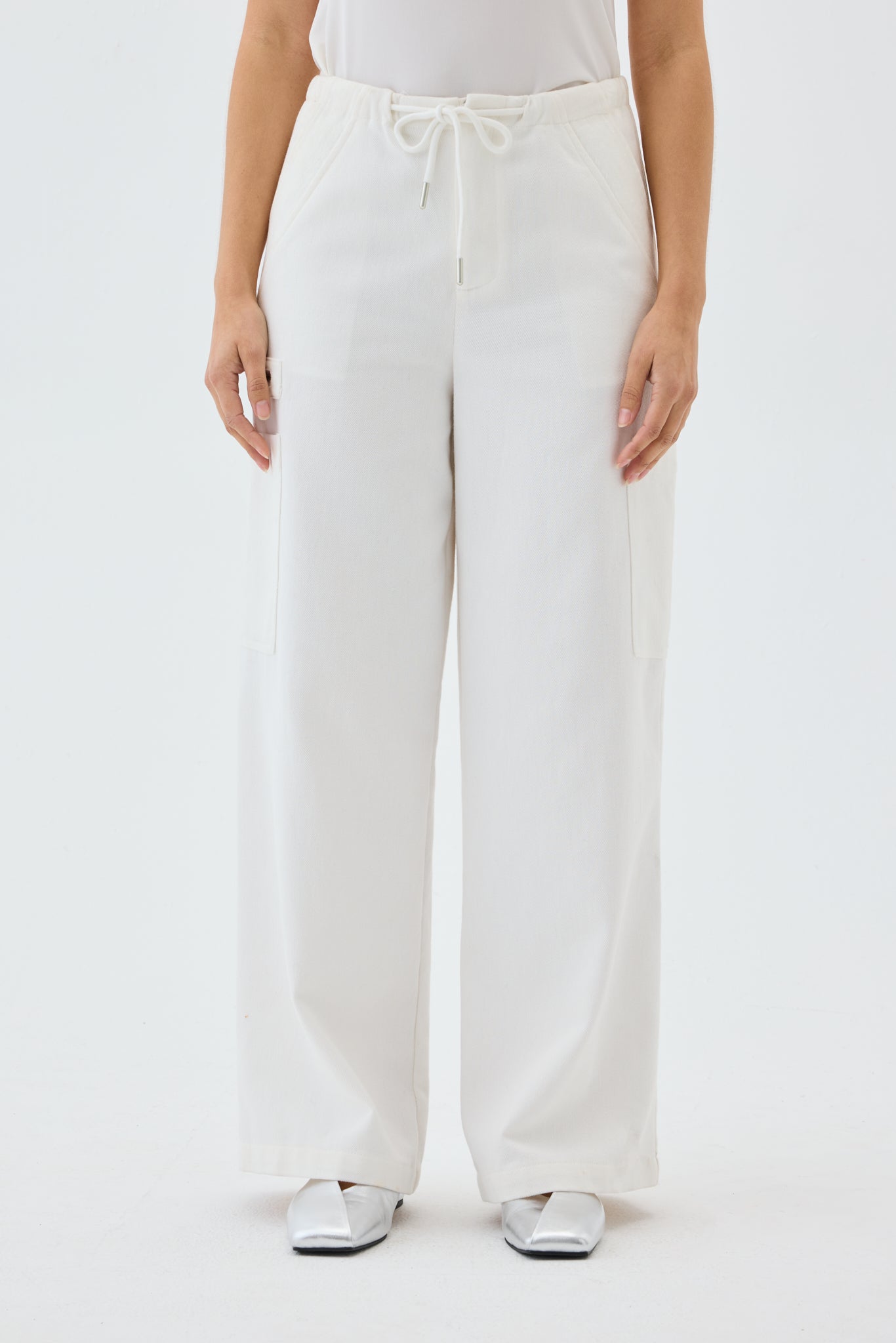 Woman wearing a white tank top and wide leg cargo pants on a light gray background