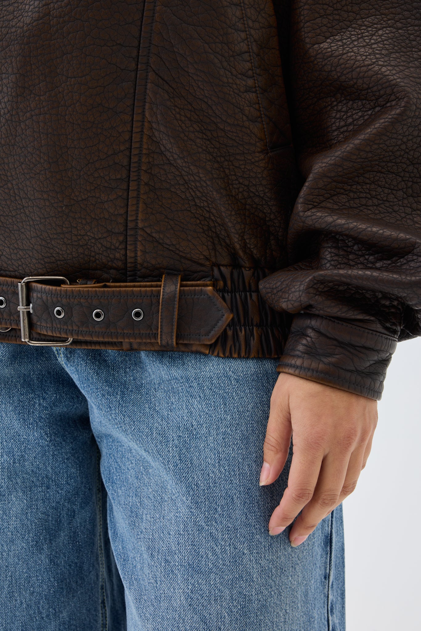 Brown leather jacket with a belt and blue jeans on a white background