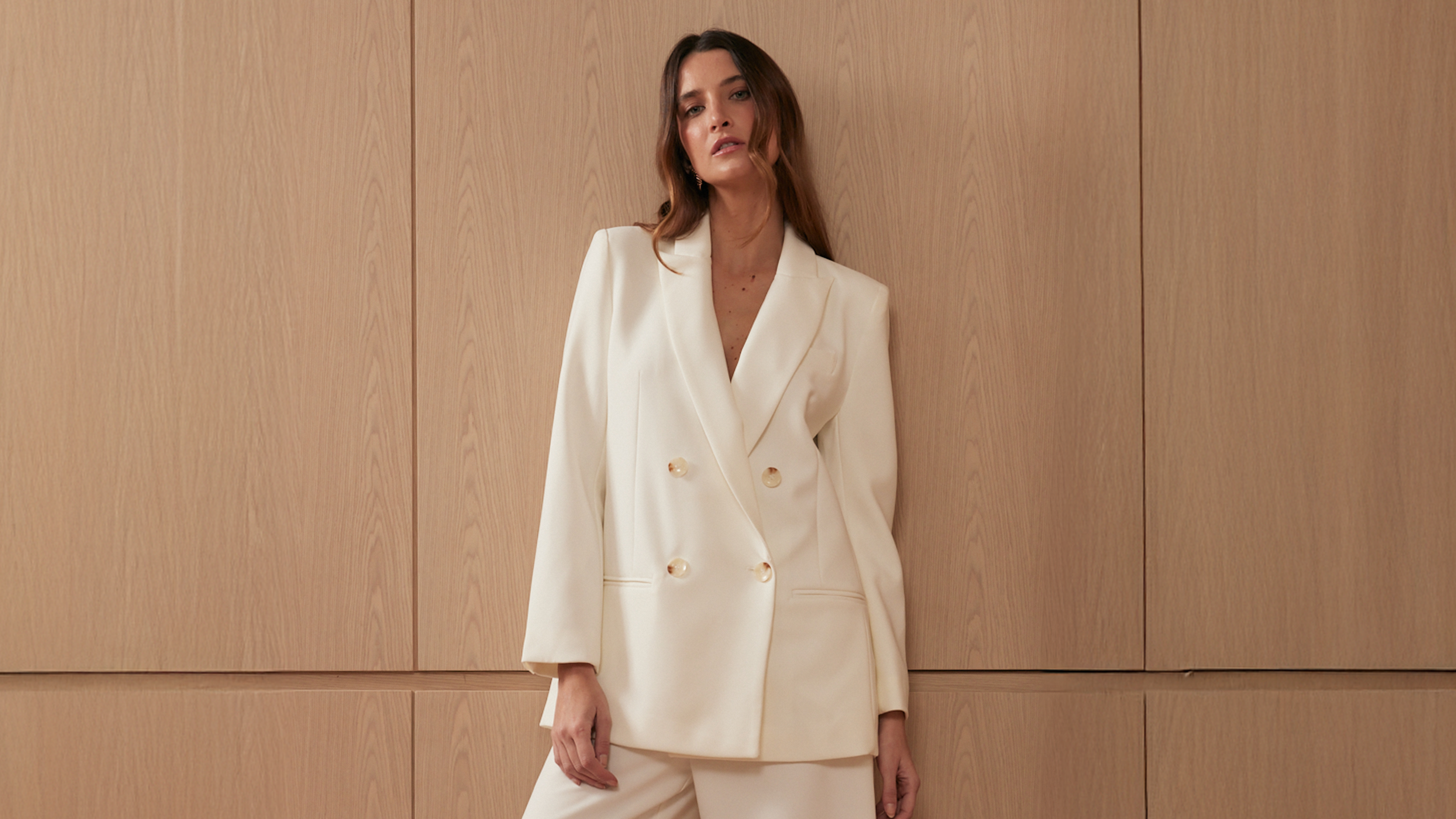Woman wearing a white suit against a beige wall