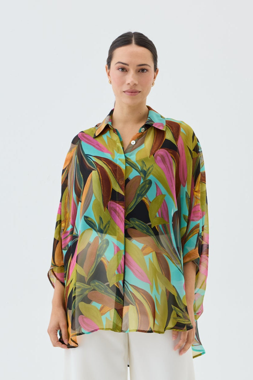 Woman wearing a colorful patterned shirt and white pants on a white background