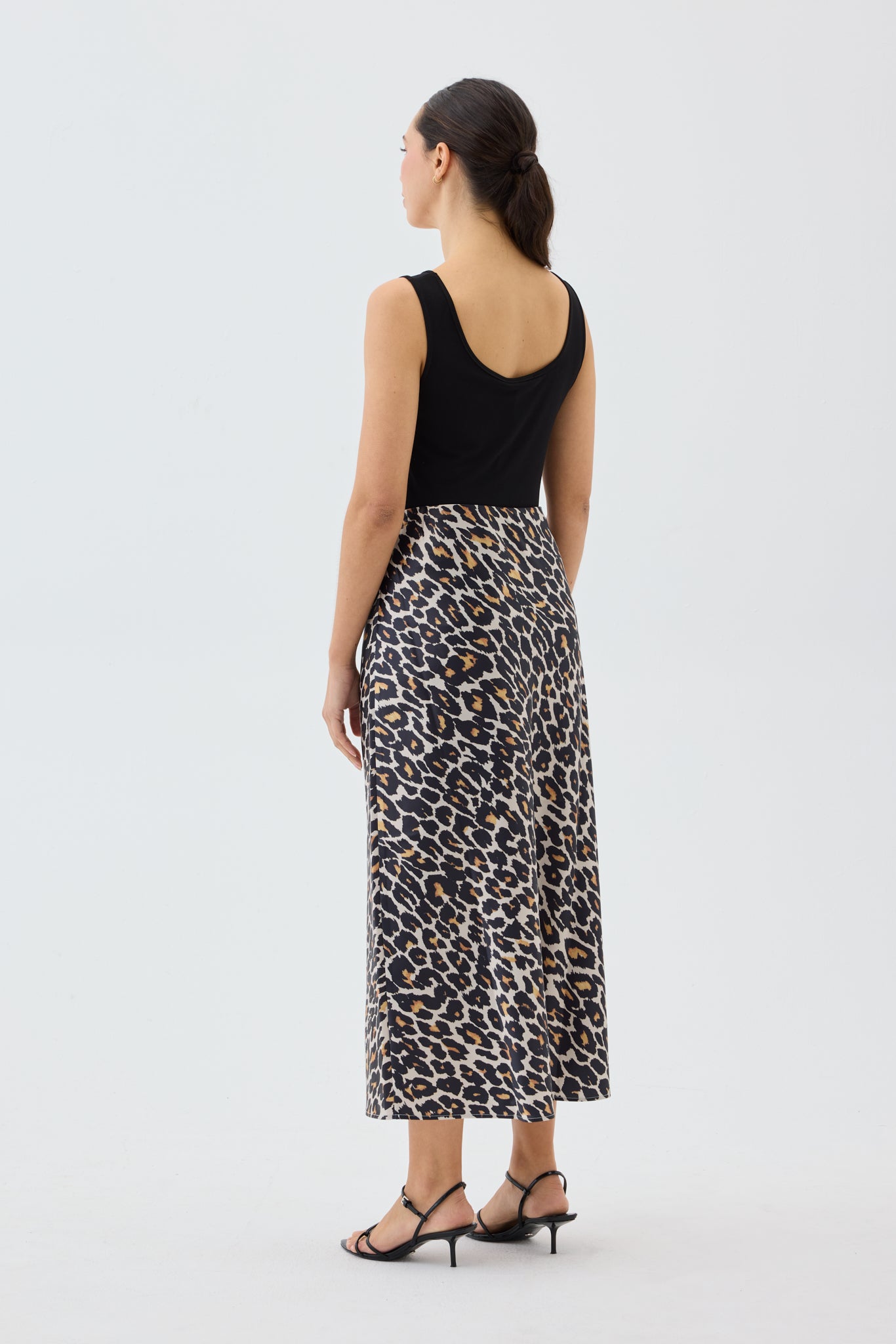 Woman wearing a black sleeveless top and leopard print skirt on a white background