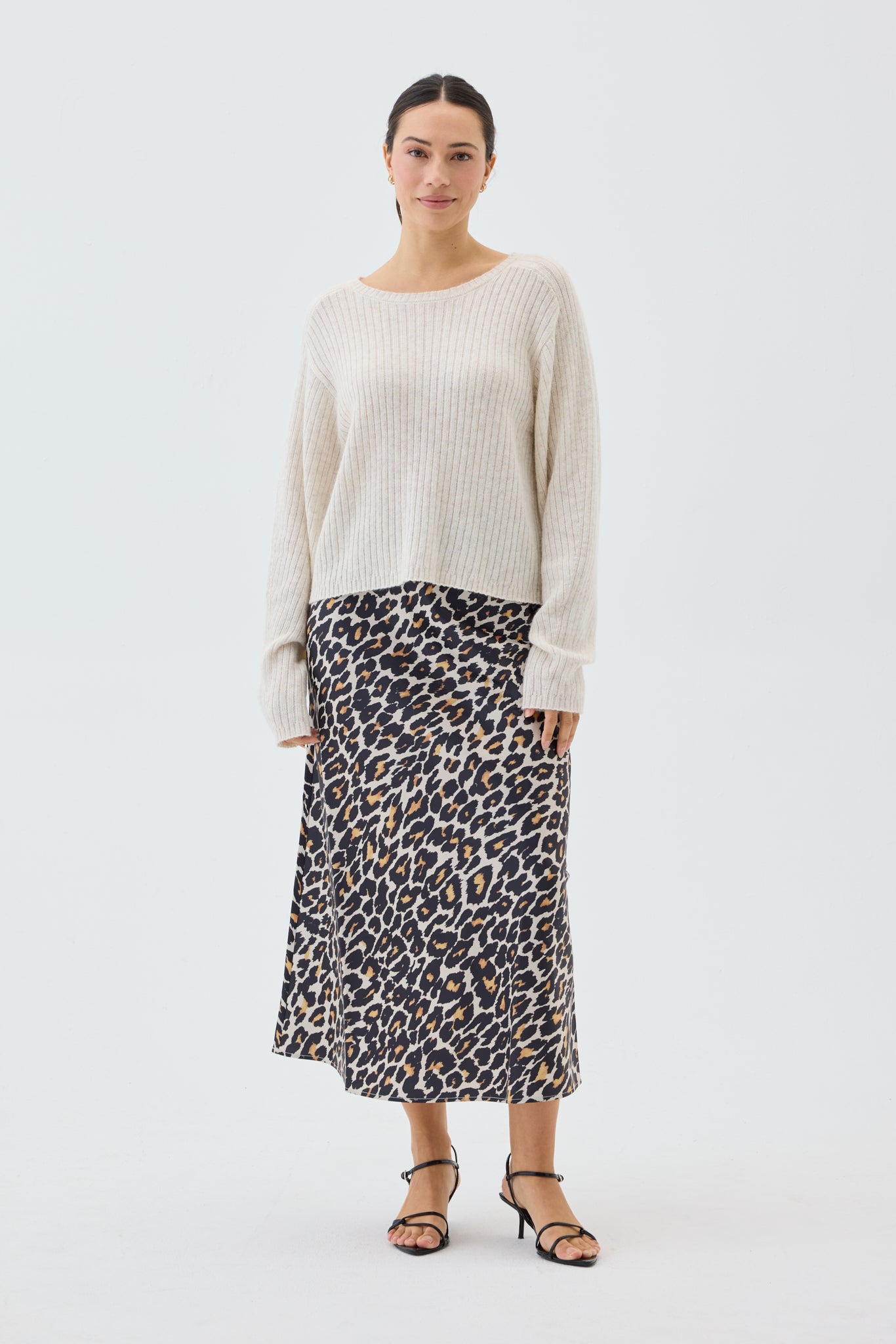 Woman wearing a beige ribbed knit sweater and leopard print skirt on a white background