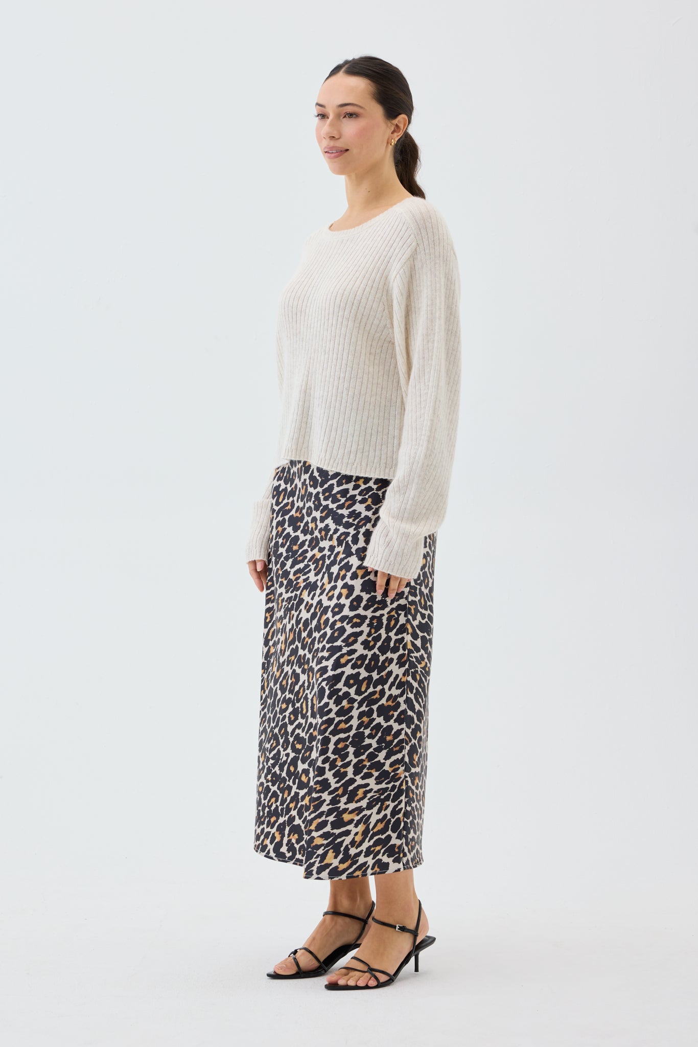 Woman wearing a beige ribbed knit sweater and leopard print skirt on a white background