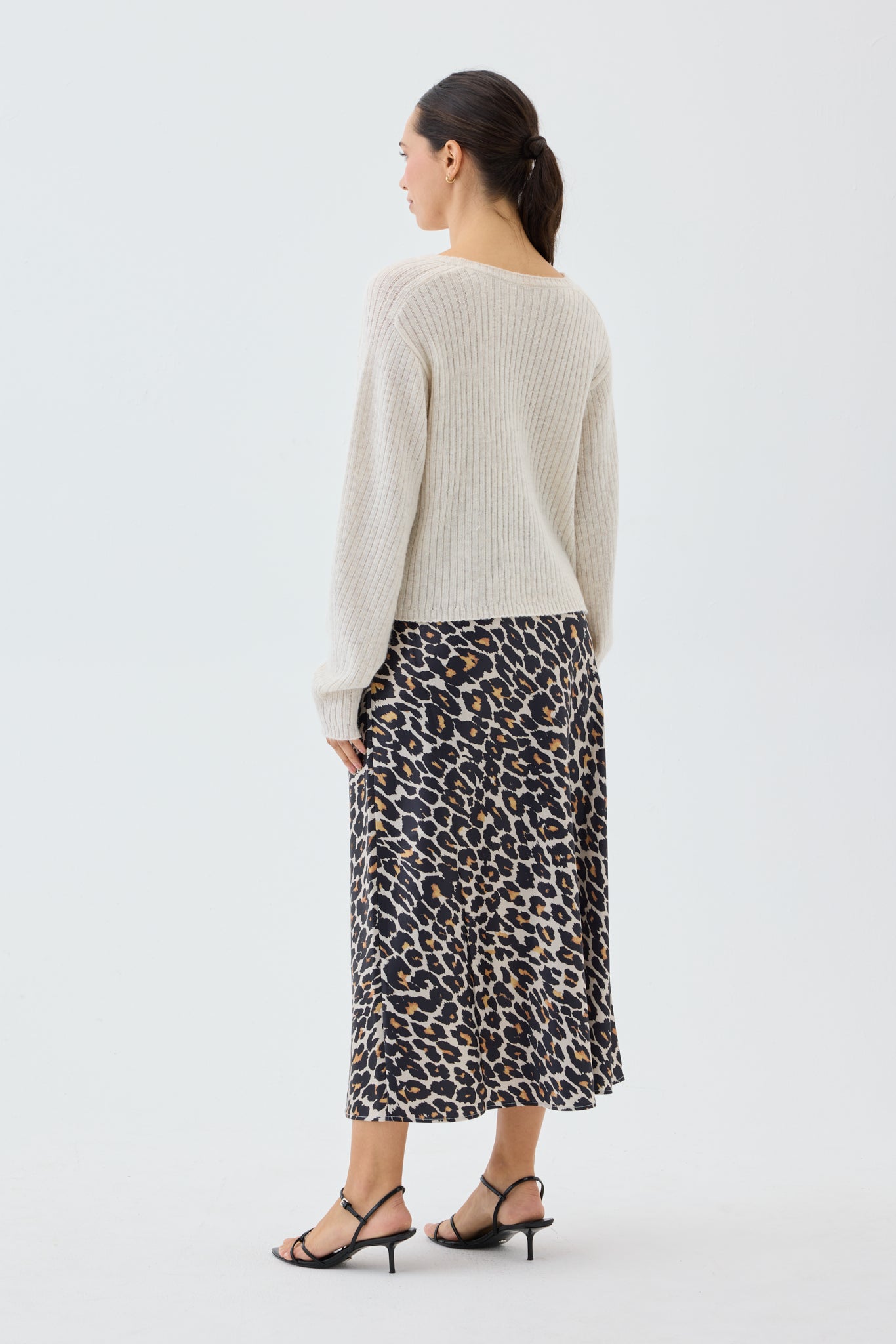 Woman wearing a beige ribbed knit sweater and leopard print skirt on a white background