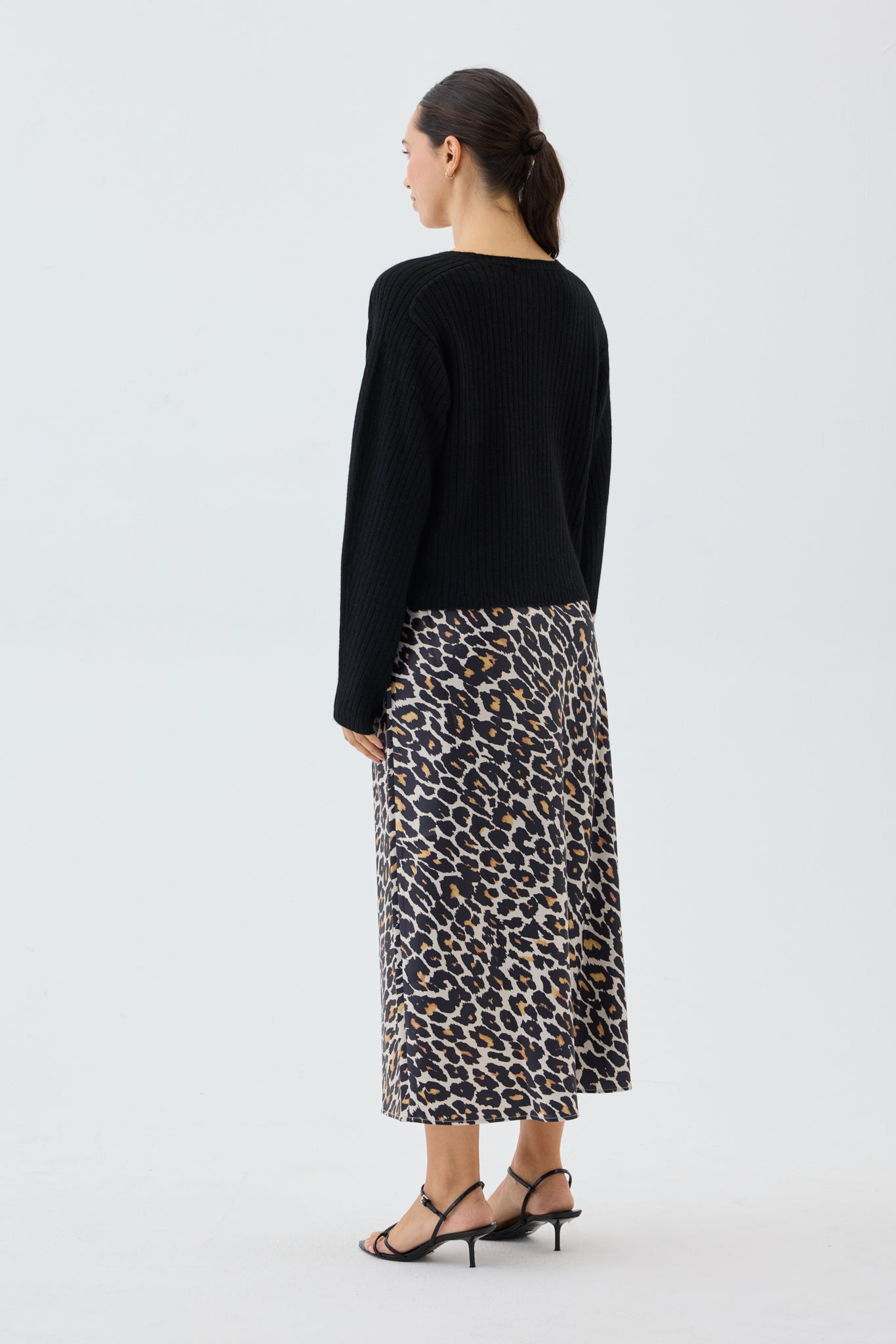 Woman wearing a black ribbed knit top and leopard print skirt on a white background