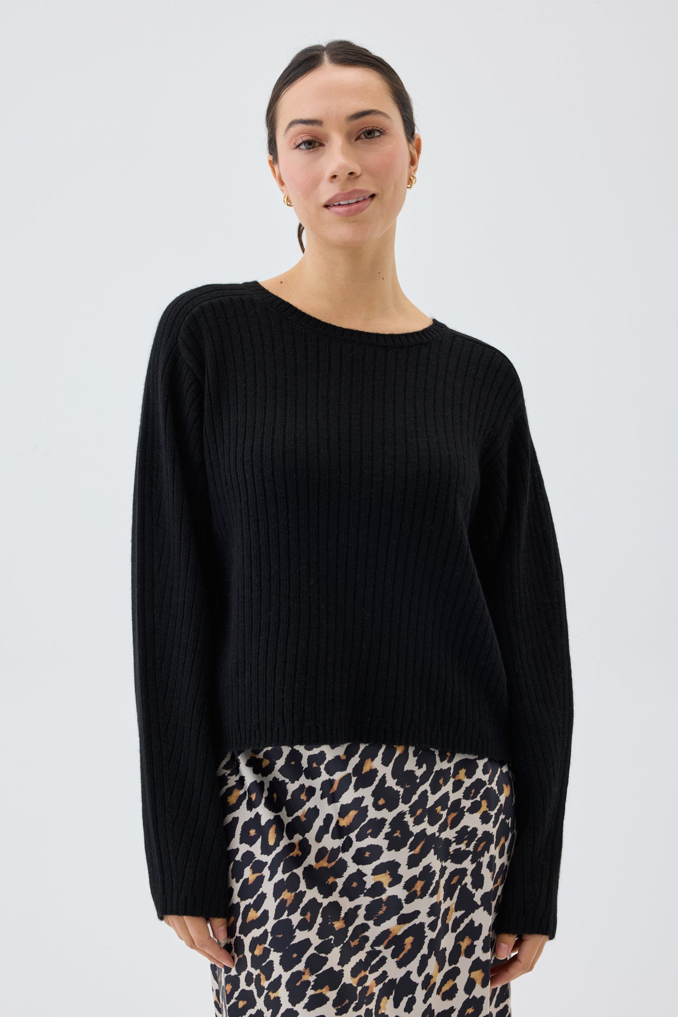 Woman wearing a black ribbed knit sweater and leopard print skirt on a white background
