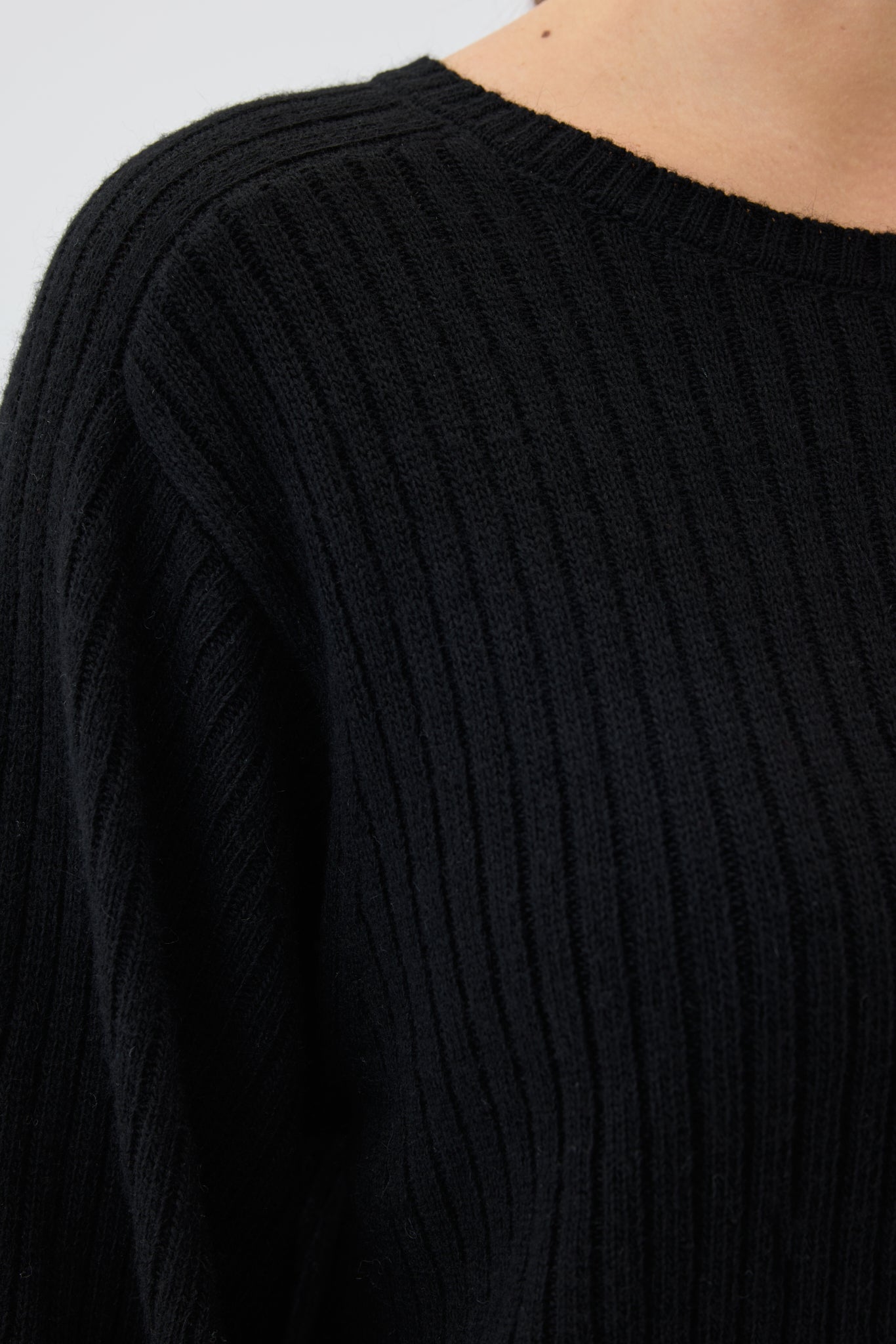 Close-up of a black ribbed knit sweater with a blurred background