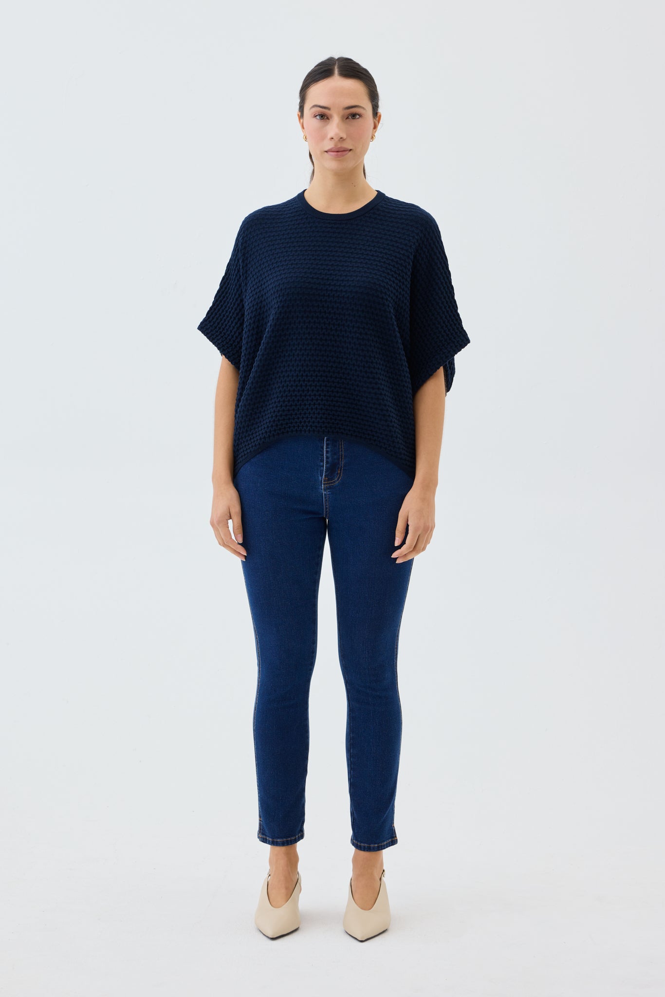 Woman wearing a navy blue top and jeans on a white background